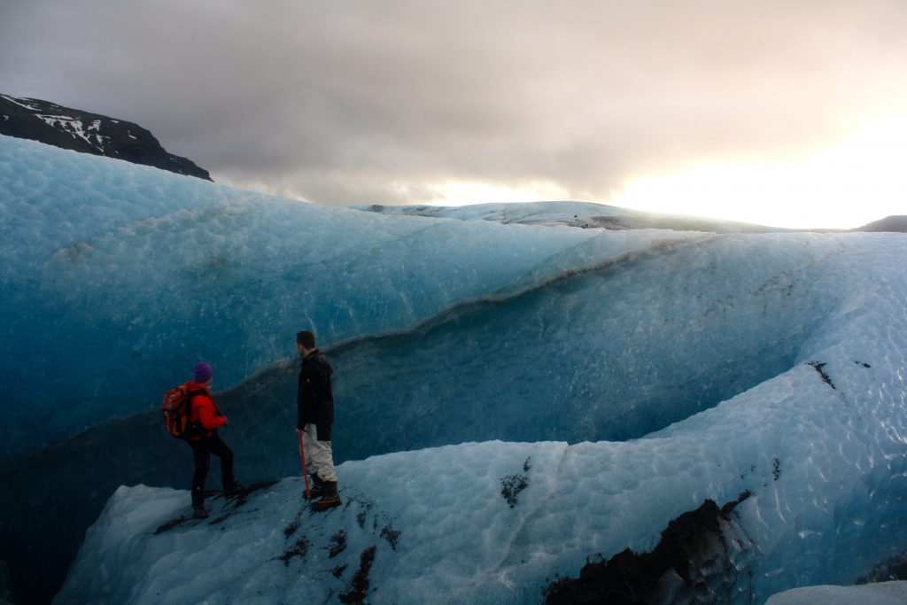 Photo: scientists walk up the shoulder of a pockmarked glacier